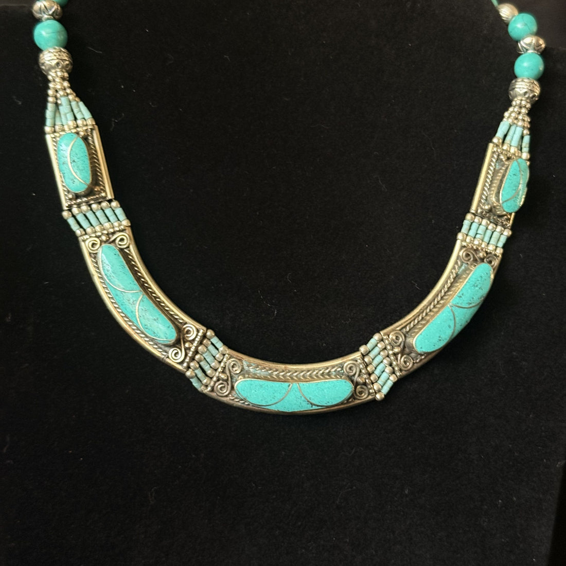A silver-toned Southwestern-style necklace featuring turquoise inlay and small round turquoise beads, displayed on a black background.