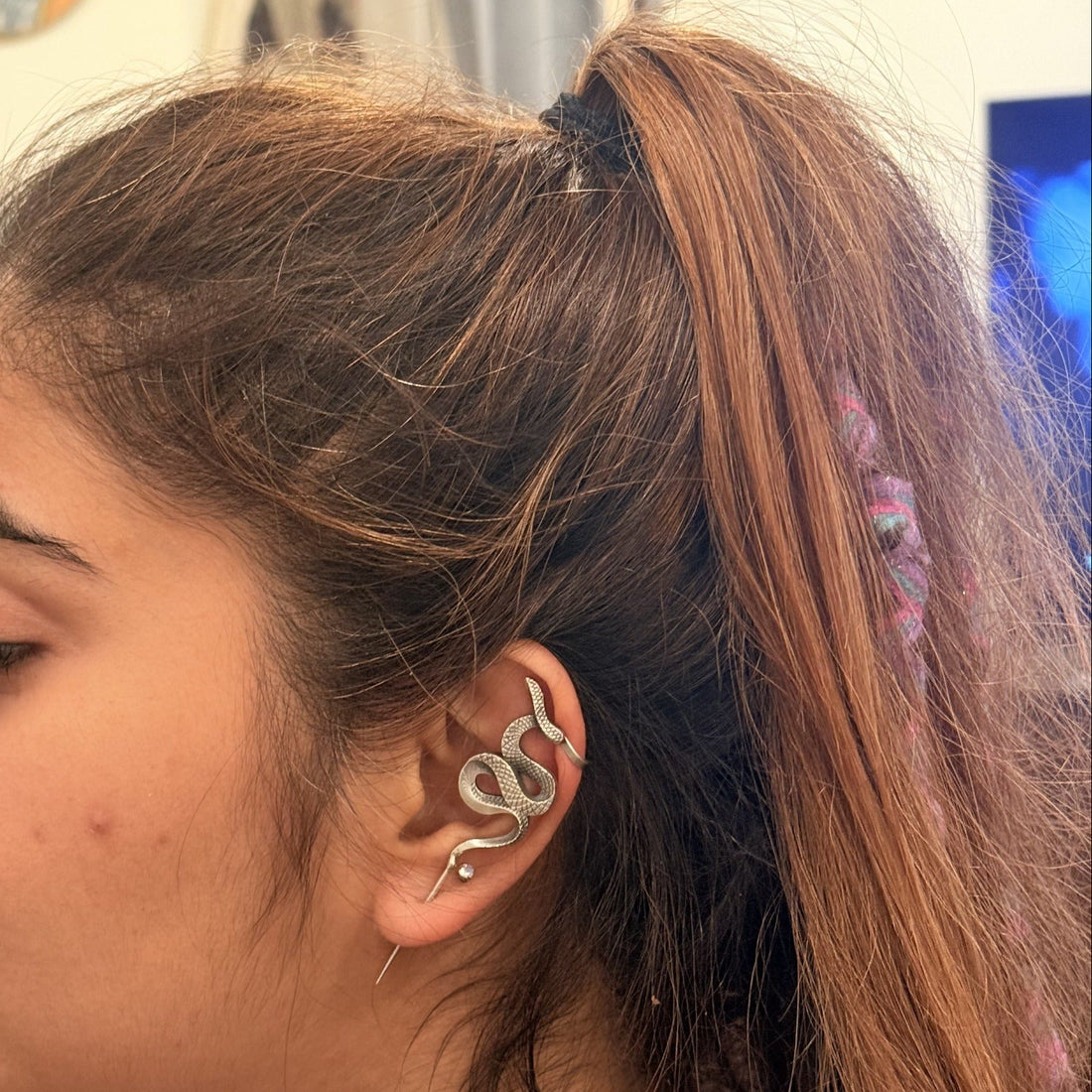 Model wearing a sculptural silver-tone snake ear cuff with clear stone accents