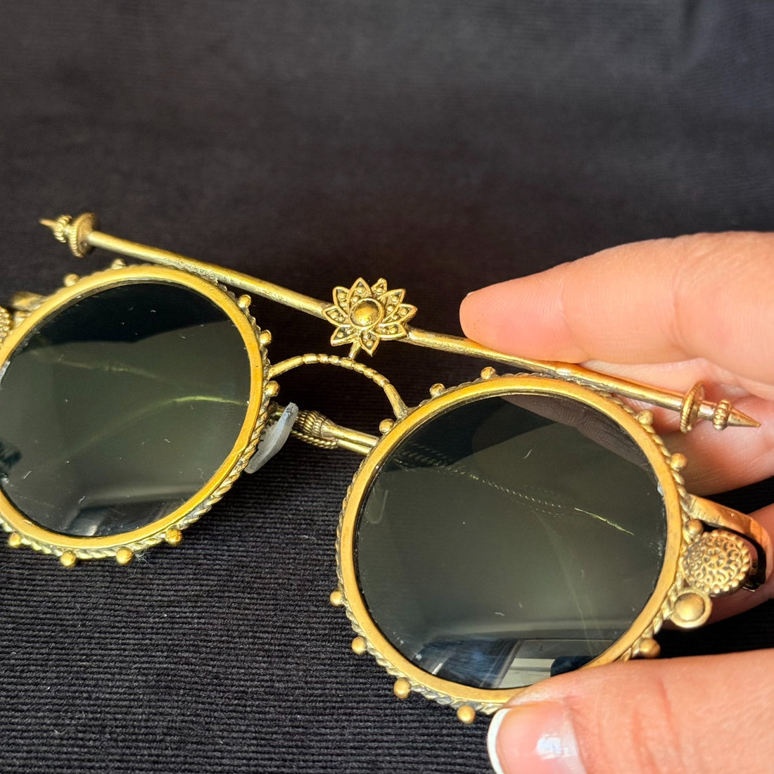 Round dark-lens sunglasses with warm brass-tone ornamental frame, lotus top bar, and sculptural side details