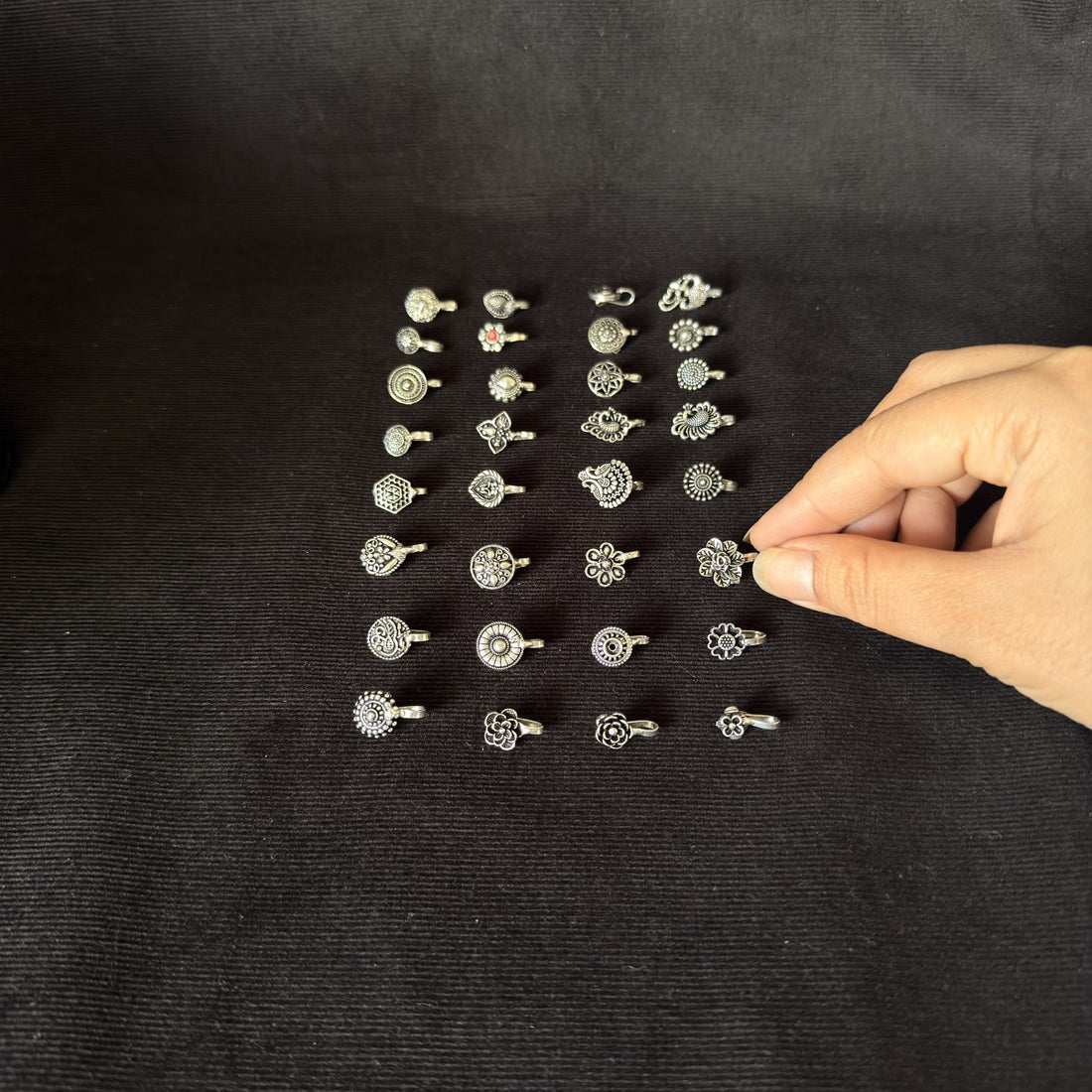 Assorted silver-tone anti nose rings and ear cuffs arranged on black fabric