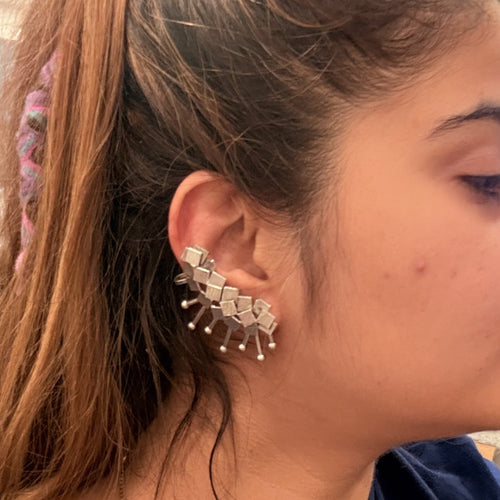 Model wearing a silver-tone geometric spike ear cuff with square stone accents and dangling pin details