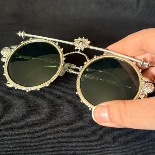 Round dark-lens sunglasses with silver-tone ornamental frame, lotus top bar, and sculptural side details